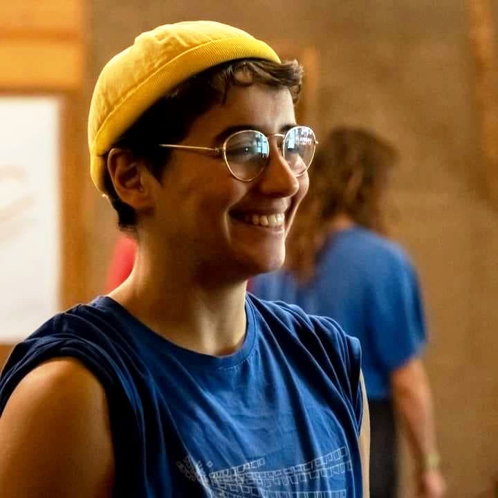 Oliver Artur smiling, wearing glasses and a yellow hat.